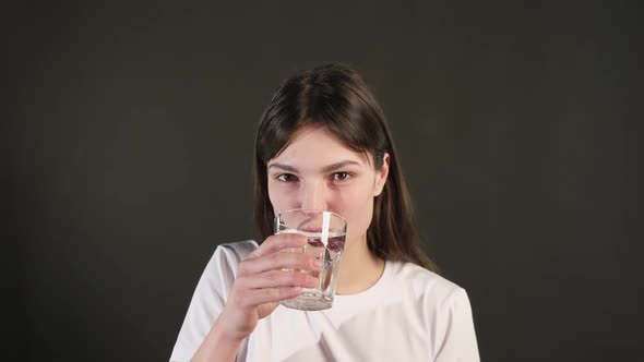 a young girl holds a glass and drinks fresh, clean, filtered mineral water. alt