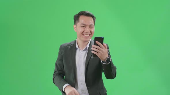 Asian Business Man Having Video Call On Mobile Phone While Walking On Green Screen Chroma Key alt