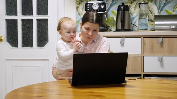 Young woman holding tiny girl and talking on a video link, baby look at laptop alt