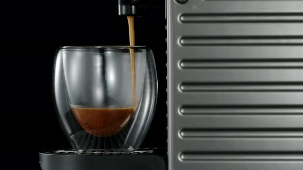 Black coffee machine pouring hot drink into the glass cup alt