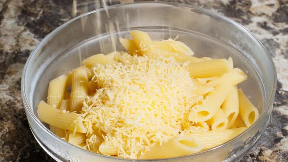 Grated cheese falling on plate with Italian penne rigate pasta. Cheese fell in the deep transparent