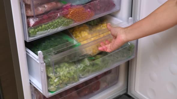 Female Hands pulls frozen corn out of the fridge. Frozen fruits, vegetables, meat in the freezer.