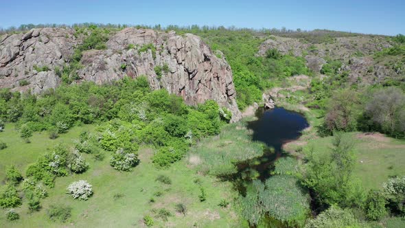 Aerial View of a Big Rock Formation and a Blue Pond Among the Greenery alt