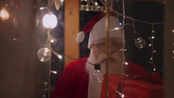 Portrait of Santa Claus Looking Out the Window and Putting His Finger to His Face and Saying Shh alt