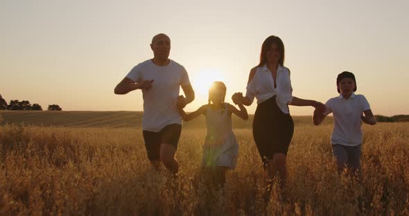 A Family With Children Is Having Fun And Running Across The Field Holding Hands