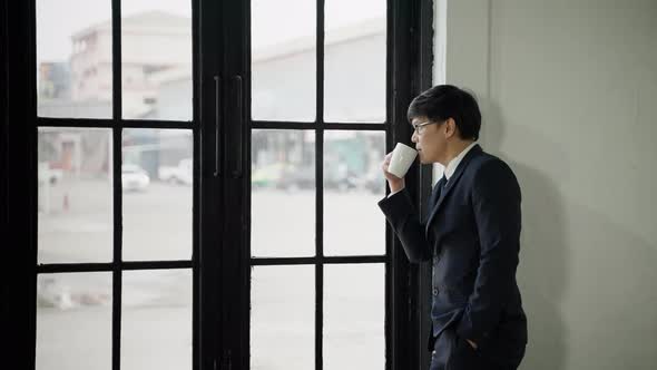 businessman or office worker standing by the window sipping coffee