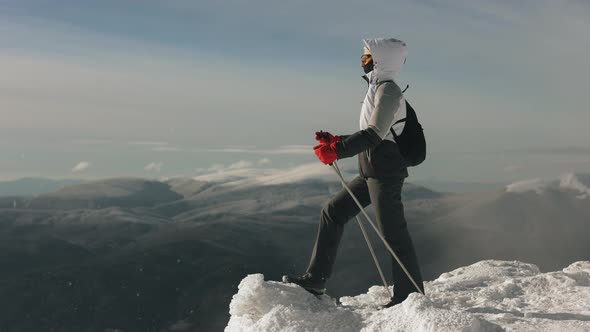 A Young Woman is Standing on the Edge of a Snowcovered Cliff and Looking at the Landscape alt
