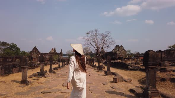 Young woman in vietnamese hat walk in Vat Phou ruined Khmer Hindu Temple, Ancient culture Laos. Slow alt