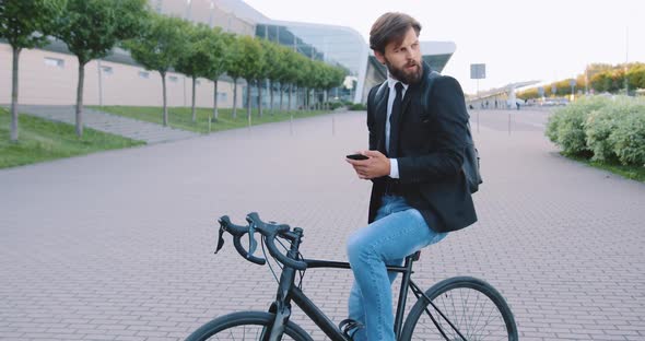 Office Worker which Sitting on His Bike and Using Phone on the Big Urban Building Background alt