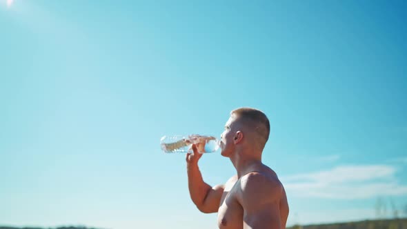 Muscular sportsman with a bottle of water in open air. alt