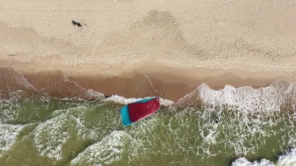 AERIAL: Top View Shot of Surfer Stranded on Sandy Beach with Crashing Waves alt