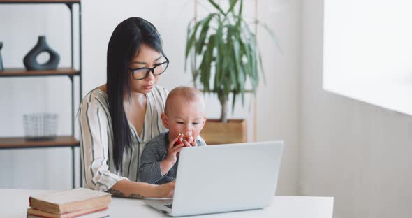 Young Mother Freelancer with Her Child Working at Home Office Using Laptop alt
