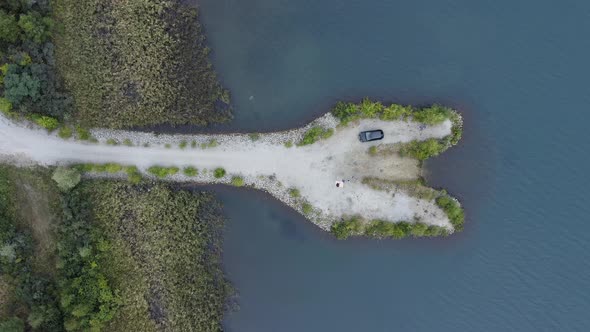 White sanded penisula in a lake with a picnicing coucle and a parked car from above - time for roman alt