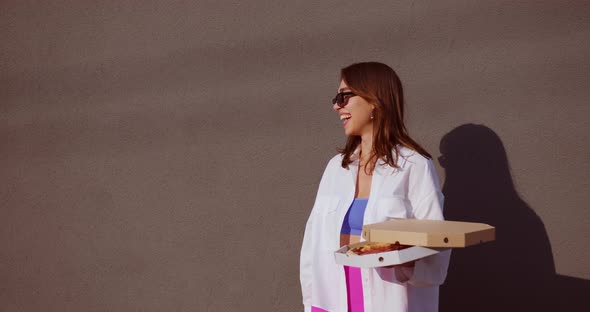girl holds a pizza in her hands and smiles, then adjusts her sunglasses alt