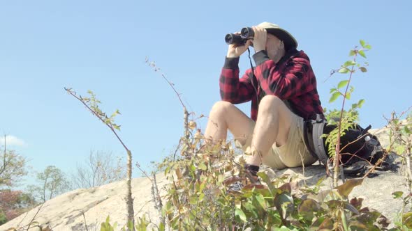 An older hiker looking through binoculars while on a scenic hike in the mountains. alt