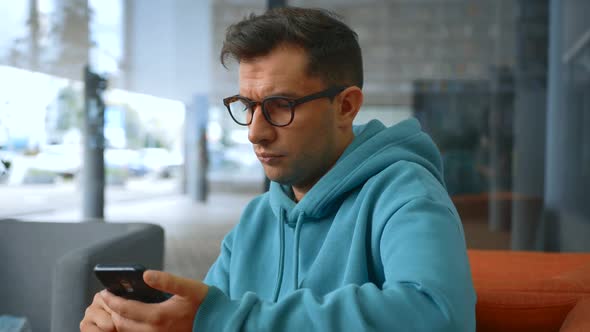 Closeup Shot of a Young Successful Programmer Wearing Glasses Checks Email on His Smartphone While