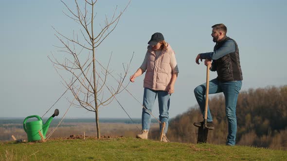 Couple of Volunteers Discussing Something While Standing Next to a Planted Tree alt
