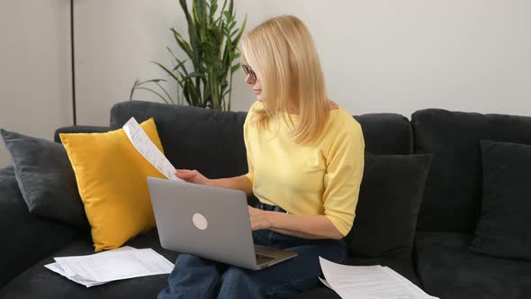 Confident 50s Middleage Female Employee Using Laptop for Remote Work Sitting on the Sofa at Home alt
