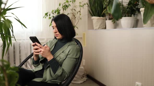 Woman chatting using smartphone, sitting on armchair at home