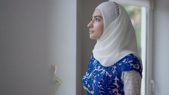 Confident Serious Middle Eastern Bride in Hijab and Wedding Dress Looking Out the Window Turning to alt
