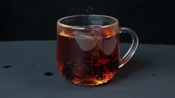 In a Transparent Cup of Black Tea Currant Berries Fall From Above