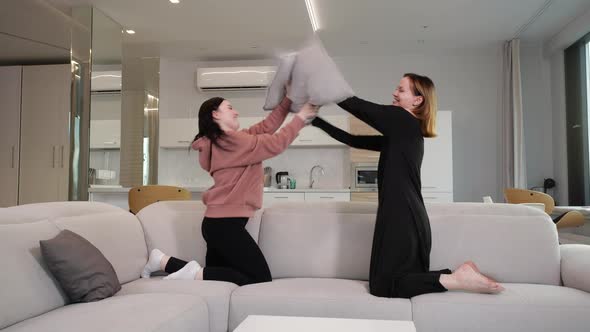 Young Girls Cheerfully Fight Pillows at Home on the Couch