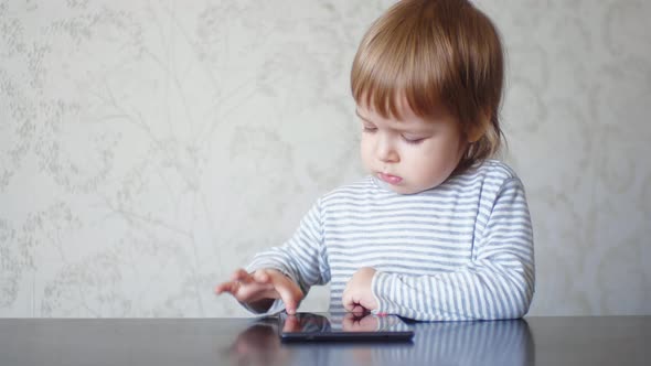 Funny Caucasian Little Boy Using Tablet Sitting at Table
