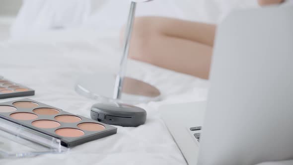 Hands of woman with learning makeup with brush on cheek on laptop computer with tutorial course. alt