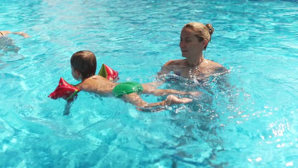 Mom in Bikini Plays with Baby in Oversleeves and His Sister in a Pool of Clear Water alt