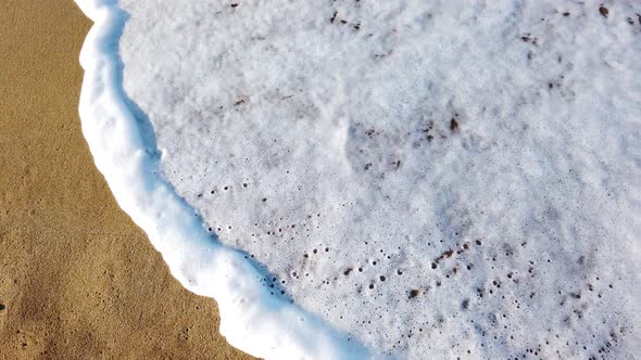 Top view of the sandy beach and white foamy waves run onto the sand.