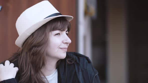 Portrait of a Happy Brunette Woman Wears a Hat Near the House and Looks Around alt