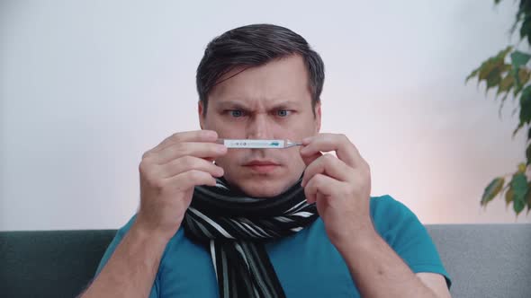 A man does not feel well looking at a thermometer. Close-up.