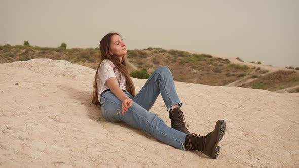 Relaxed Woman with Long Hair and Jeans Lies on Rocky Hill Slope in Cappadocia