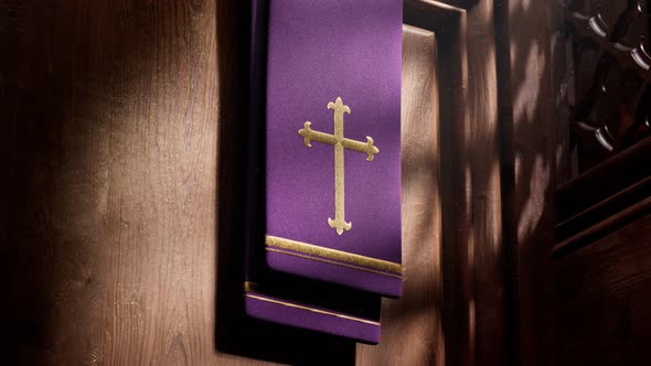 Purple stole with cross lightened by rays of light falling into a confessional. alt