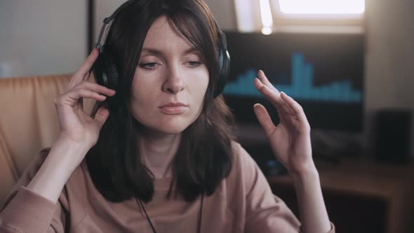 A beautiful girl with big headphones listens to music in a chair at the computer, dances
