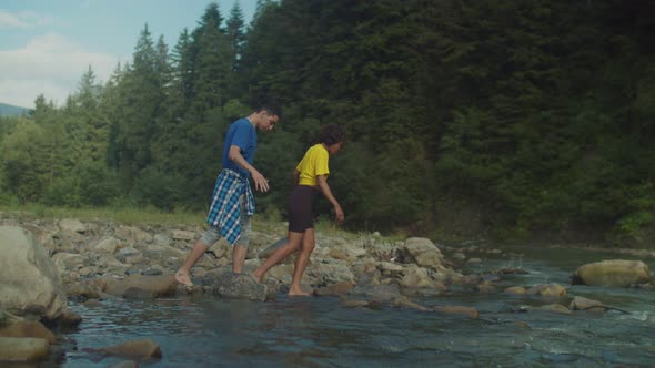 Attractive Multicultural Couple Travelers Wading Mountain River on Hike alt