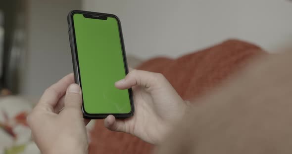 Female scrolling on smart phone with green screen, lying on sofa at home