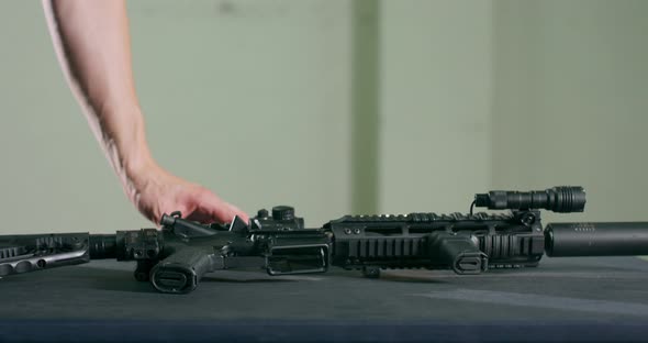Closeup of a Man Examining and Picking Up a Gun Magazine Clip and an Assault Rifle From a Table alt