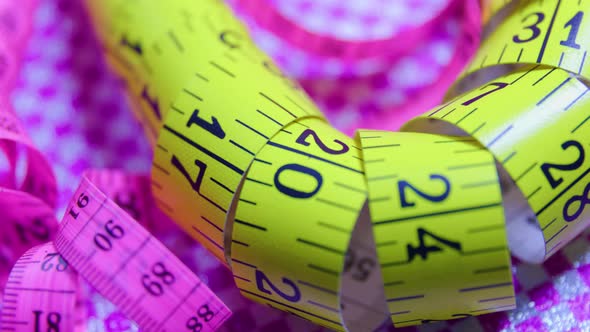 Close Up of a Pink and Yellow Measure Tape on Colored Rotating Background alt