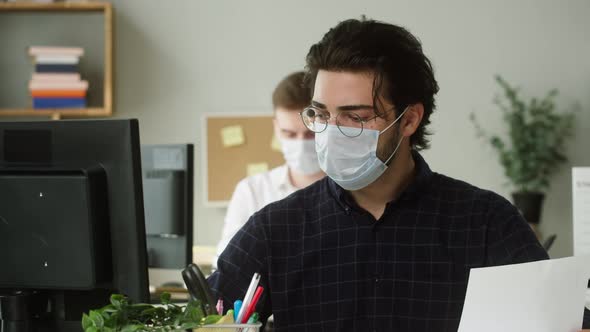 Serious Darkhaired Man in Circle Glasses Wearing Medical Mask Concentrated on Work in Office alt