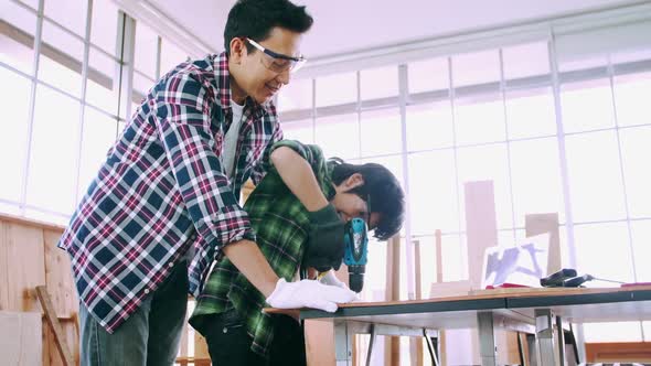 Young male carpenter teaching his son how to work with wood in workshop. alt
