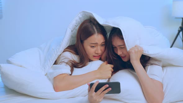 Asian attractive lesbian couple  lying down with blanket use mobile phone watch movie on bed. alt