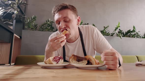 European Man Appetizingly Eating Fresh Croissant with Chocolate Filling in Coffee Shop alt