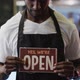Portrait of happy african american barista holding 'we're open' sign in cafe - VideoHive Item for Sale