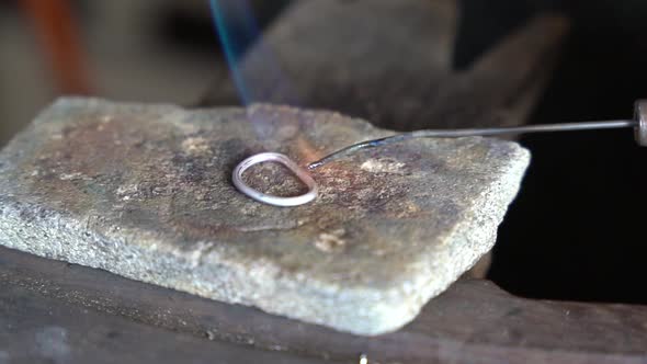 Torch heating and melting precious metal ring for creating an art piece, Close up view alt