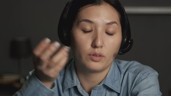 Close-Up of a Young Asian Woman in Headphones with a Microphone Communicating alt