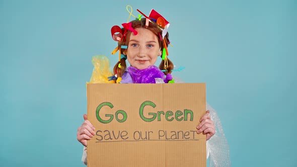  Girl with plastic trash on herself holding cardboard with inscription