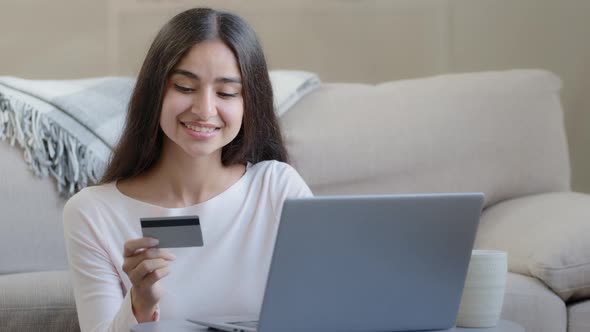 Happy Female Arabian Consumer Shopper Hold Plastic Banking Card Enter Numbers for Online Bank App alt