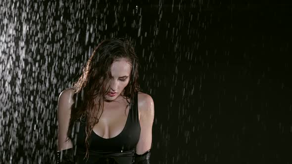 Portrait of a Beautiful Woman in a Black Suit Posing Against a Dark Background While Raindrops Pour alt