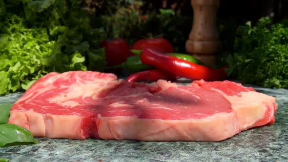Raw Steak is Falling on a Stone Table on the Background of Fresh Vegetables alt